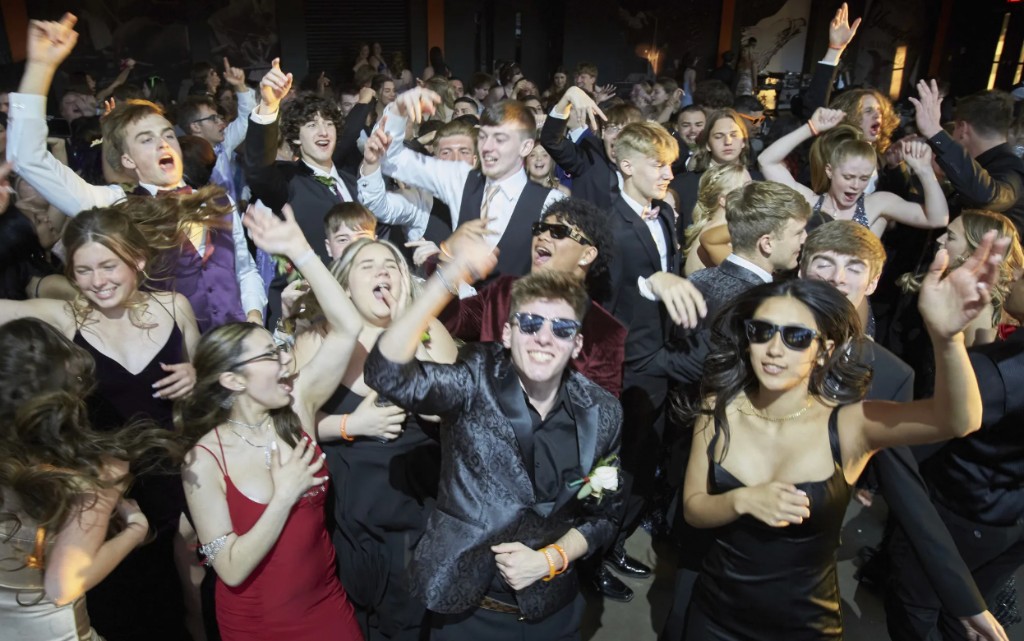 College students in formal attire packed on a dance floor with hands in the air.