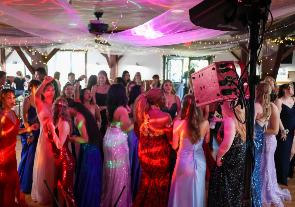 High school students in formalwear dancing under pink uplighting at a winter formal.