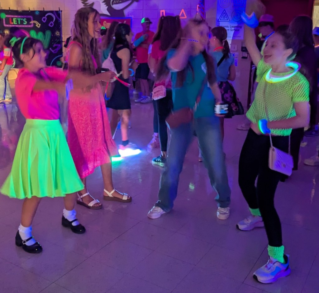 Middle school students dancing in neon and glow accessories at a school dance.
