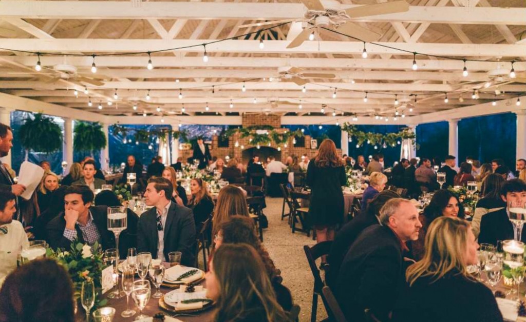 Wedding guests dining under string lights in a white pavilion during cocktail hour and dinner.